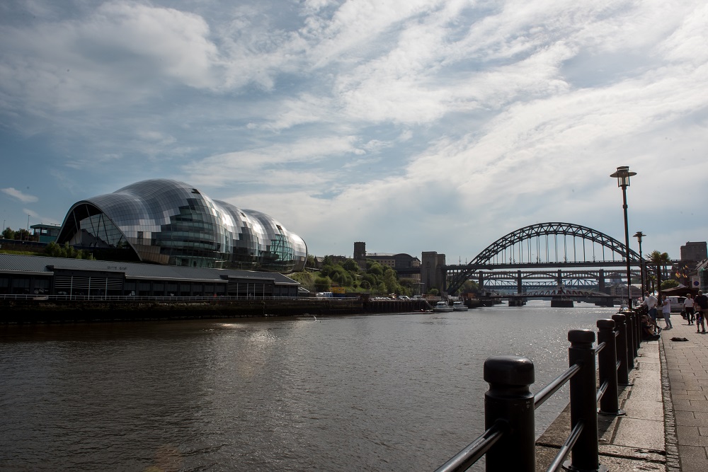 Daytime view of curves of Sage, Gateshead from opposite bank of River Tyne with Tyne Bridge to the left.